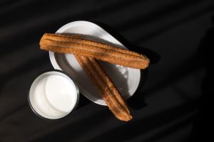 A Glass of milk and flour churros with sugar and cinnamon with space for text on the right dark background